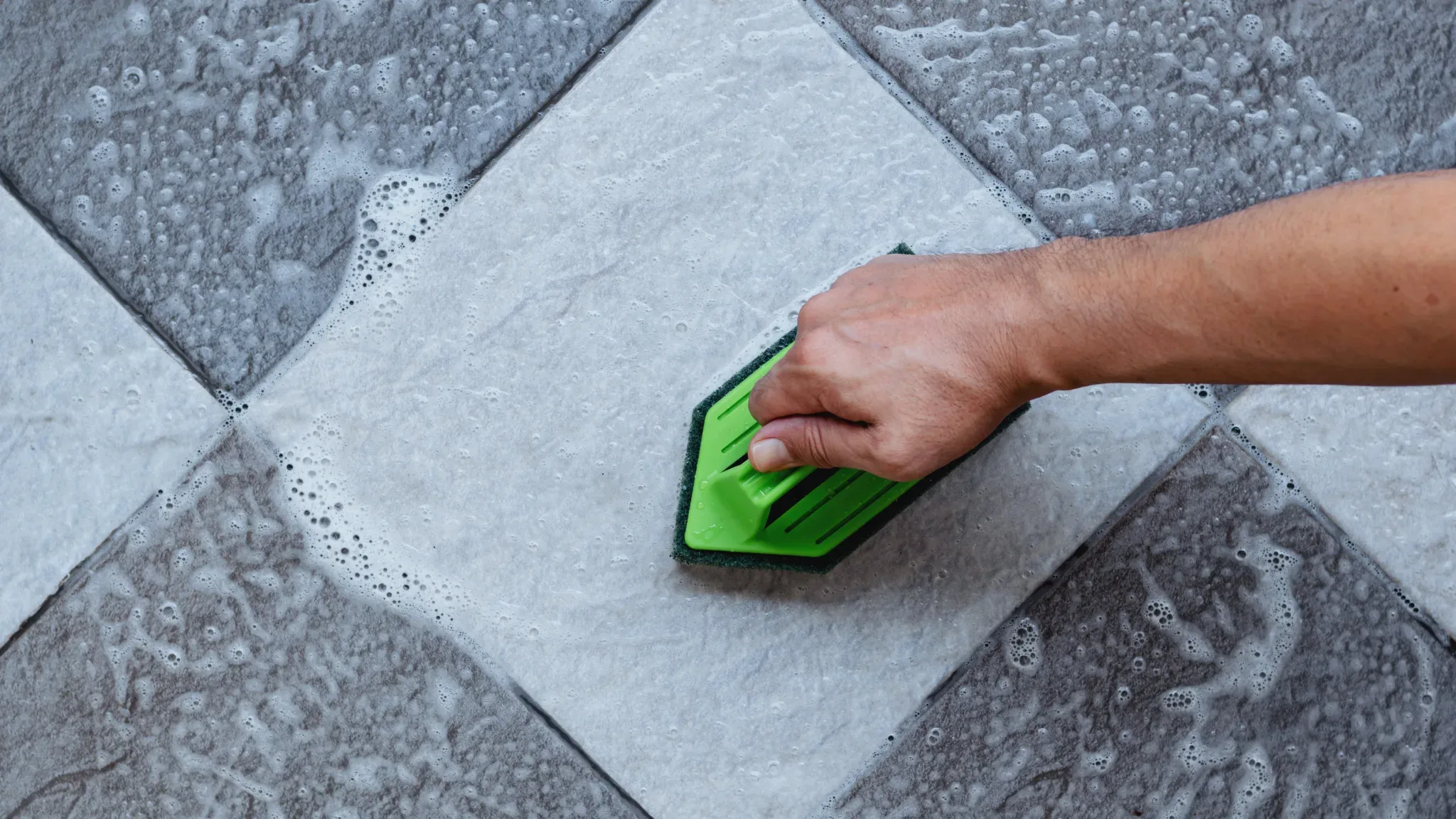 Professional cleaning and maintenance of tile flooring using a green scrubbing brush tool on wet tiles