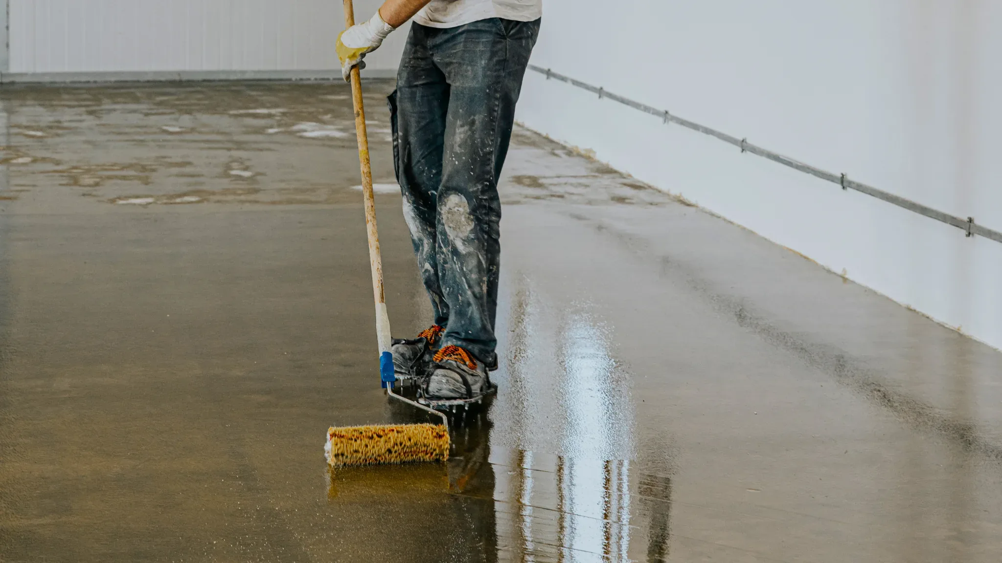 Professional worker cleaning and sealing a concrete floor with a specialized roller tool, demonstrating floor preparation and
